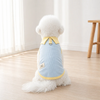 A fluffy white dog wearing a light blue cartoon dress with a yellow collar sitting on a wooden floor.