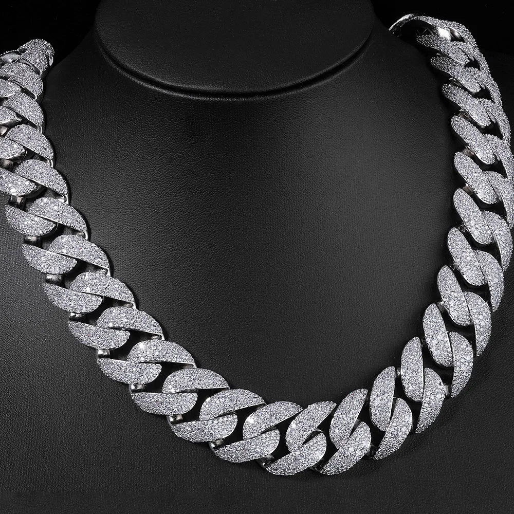 A close-up of a silver-toned Cuban link necklace with a curved flip buckle design displayed on a black display stand.