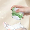 A hand is using a green pet bath brush with a built-in dispenser to apply shampoo foam onto a pet's fur.