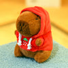 An orange capybara plush doll wearing a red hoodie with white trim and green accents.