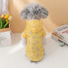 A fluffy gray dog wearing a yellow raincoat with pink patterns sitting on a white surface.