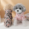 A fluffy grey dog wearing a pink cartoon printed raincoat with a hood, standing next to another light-colored dog.