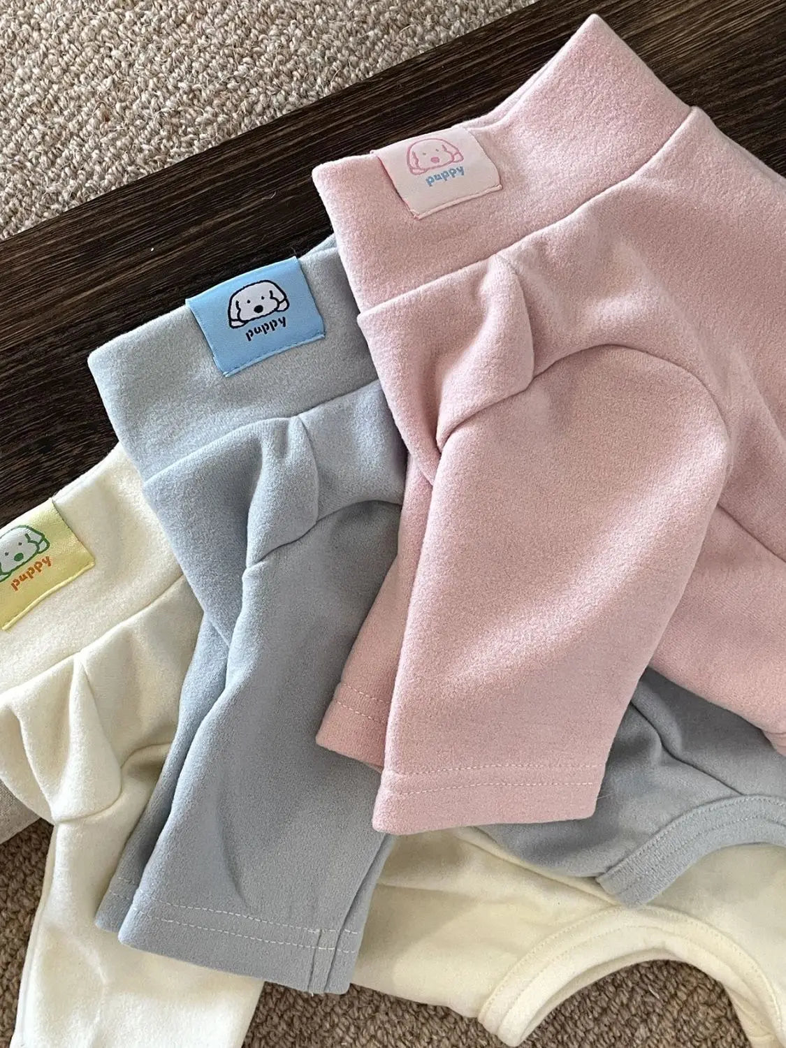 A stack of pink and gray soft stretch dog pajamas for small and medium pets with branded tags.