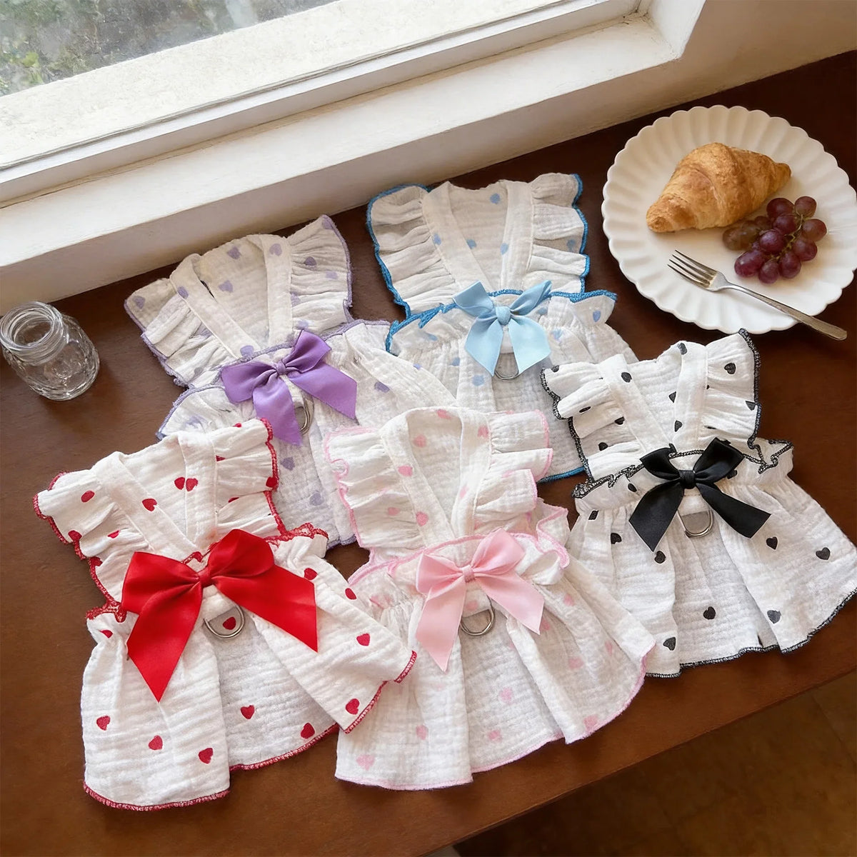 A collection of white and pink breathable summer pet dresses with various bows and details displayed on a wooden surface.