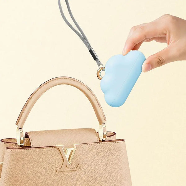 A hand holds a light blue cloud-shaped lint roller refill with a thin cord, positioned above a beige leather handbag.