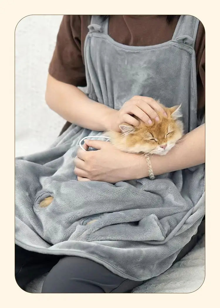 Una persona con un delantal de forro gris acaricia suavemente a un pequeño gato naranja.