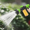 A hand sprays a garden with a green and yellow high-pressure foam cleaning gun.