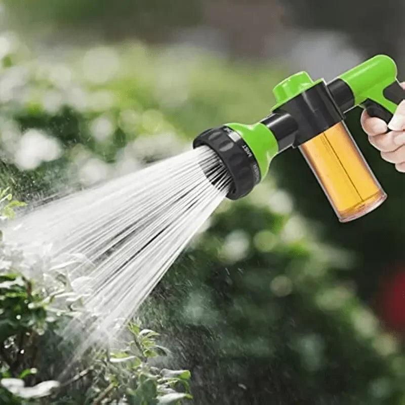A hand sprays a garden with a green and yellow high-pressure foam cleaning gun.