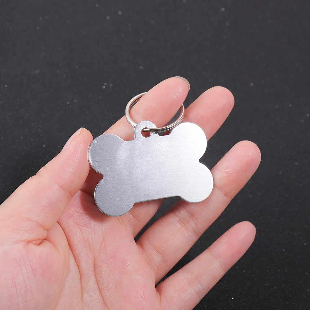Silver bone-shaped dog ID tag held in a person's hand against a dark background