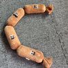 A brown squeaky dog chew toy shaped like a sausage with facial features, lying on a gray textured surface.