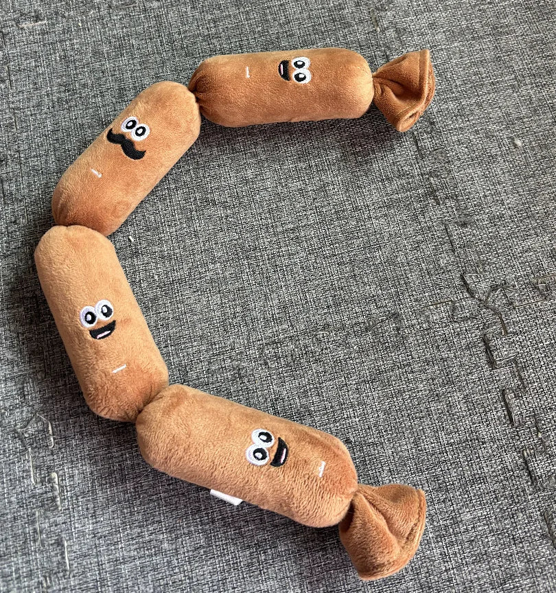 A brown squeaky dog chew toy shaped like a sausage with facial features, lying on a gray textured surface.