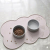 A pink non-slip pet mat features two small ceramic bowls on a light gray surface.