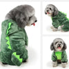 Un perro gris esponjoso vistiendo un mono de dibujos animados verde para mascotas pequeñas.