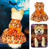 Un perro blanco esponjoso vistiendo un vestido estampado de murciélago de calabaza naranja y negra con un gran lazo.