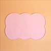 A pink silicone pet feeding mat with a scalloped edge set against a light orange background.