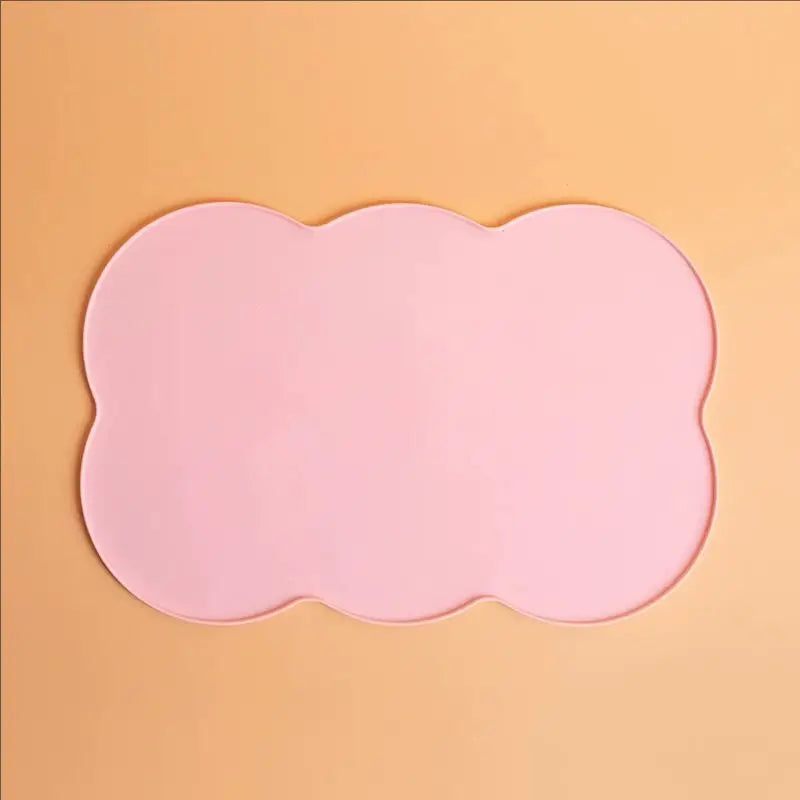 A pink silicone pet feeding mat with a scalloped edge set against a light orange background.