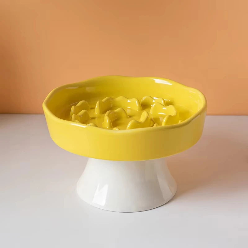 Bol en céramique jaune à nourriture, avec nourriture, sur un piédestal blanc.