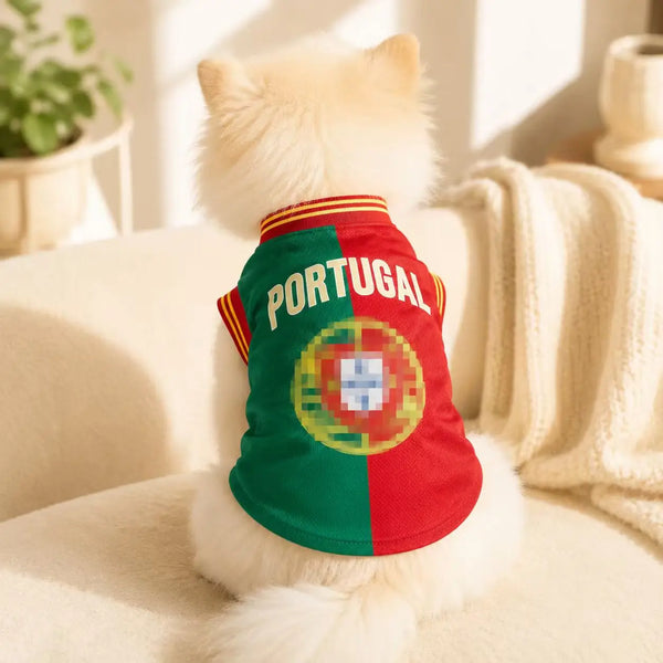 A fluffy white dog is wearing a green and red Portugal soccer jersey.