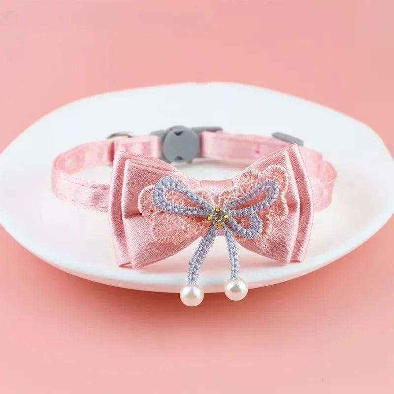 Rosa Spitzenhalsband für Haustiere mit Schleife und herabhängenden Perlen auf einem weißen Teller.