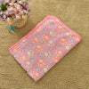 Pink fleece pet bed mat cover with multicolored paw prints resting on a beige textured surface.