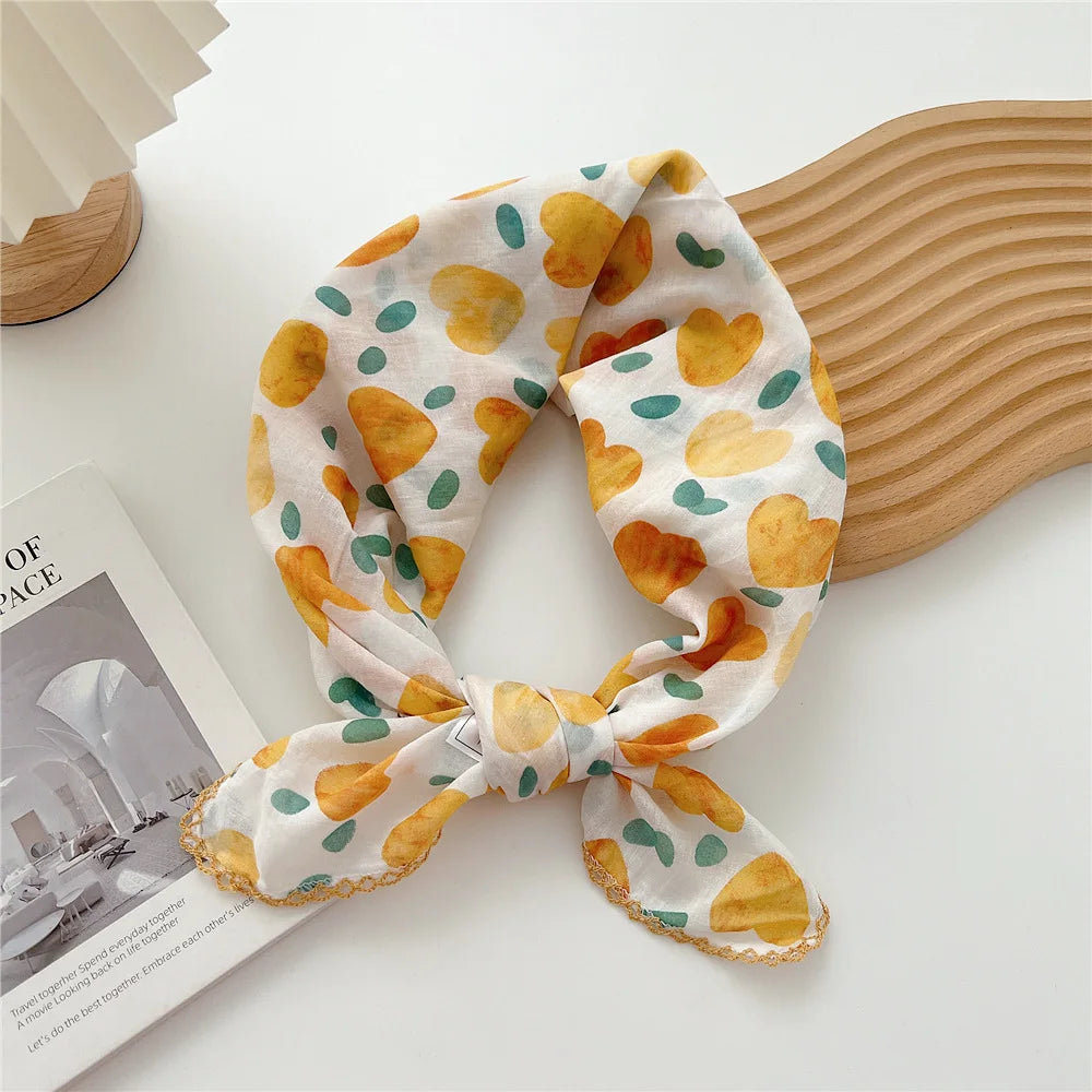 Écharpe en coton à motif floral jaune et vert, nouée en nœud, à côté d'un objet en bois.