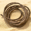 A coil of realistic artificial reptile vines lying on sandy ground.