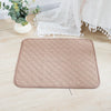 A beige, quilted reusable washable pet training mat lying on a light wooden floor next to white lace fabric.
