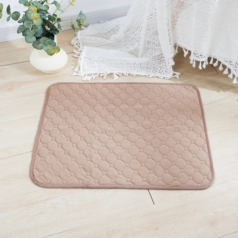 A beige, quilted reusable washable pet training mat lying on a light wooden floor next to white lace fabric.