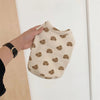 A hand holds a light beige cartoon print dog vest for spring or summer.