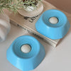 A light blue interactive slow feeder dog bowl resting on a wooden book next to a potted plant.