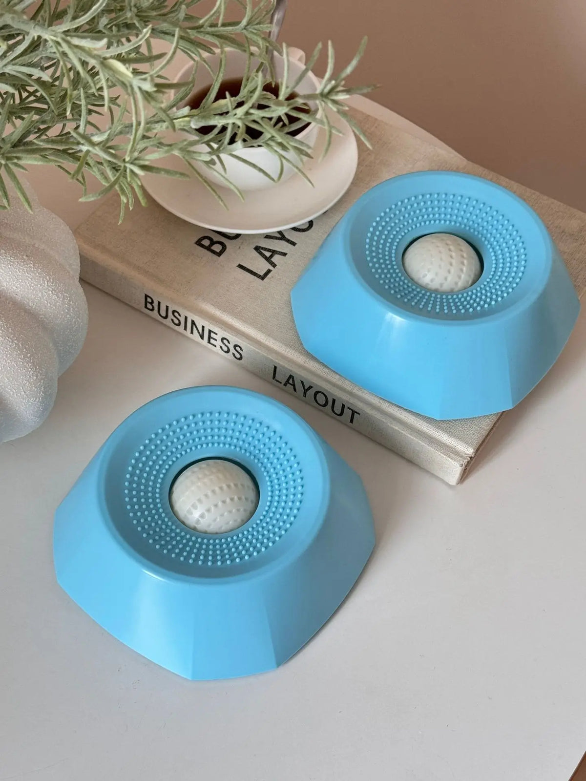 A light blue interactive slow feeder dog bowl resting on a wooden book next to a potted plant.