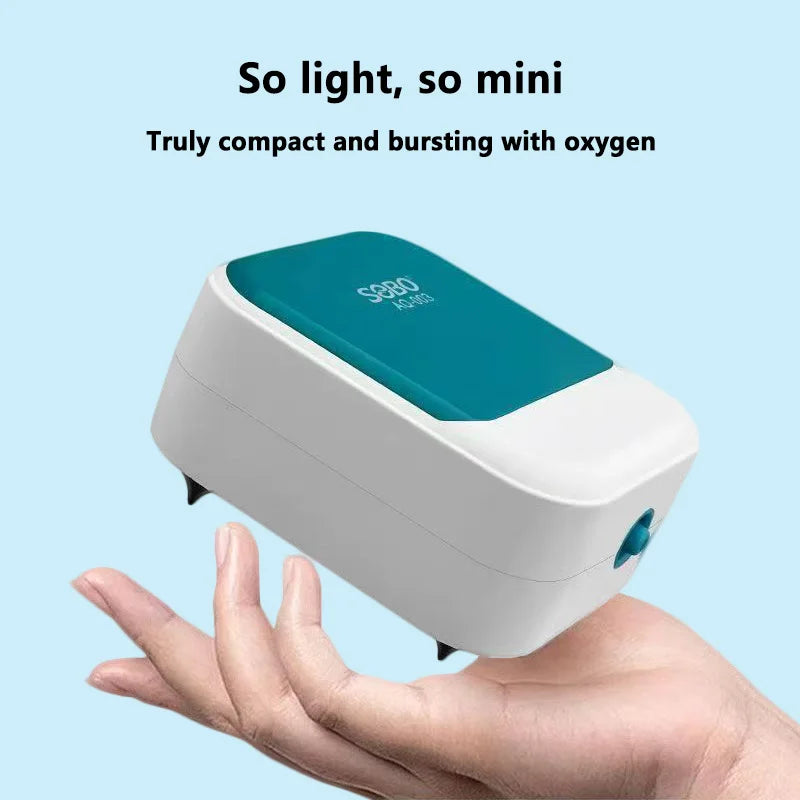 A hand holds a white and teal compact air pump for aquarium oxygenation.