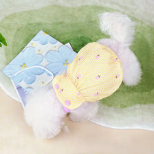 A yellow polka dot dog hat with a lace bow is displayed on a green felt background surrounded by white faux fur.