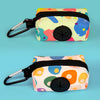 A colorful, patterned poop bag holder with a black strap and clip is shown against a light blue background.