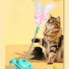 A fluffy tabby cat is interacting with an interactive toy featuring a feather wand and a rolling ball.