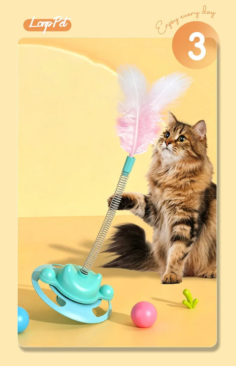 A fluffy tabby cat is interacting with an interactive toy featuring a feather wand and a rolling ball.