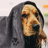 A golden-colored dog peeks out from under a dark gray pet bath towel.