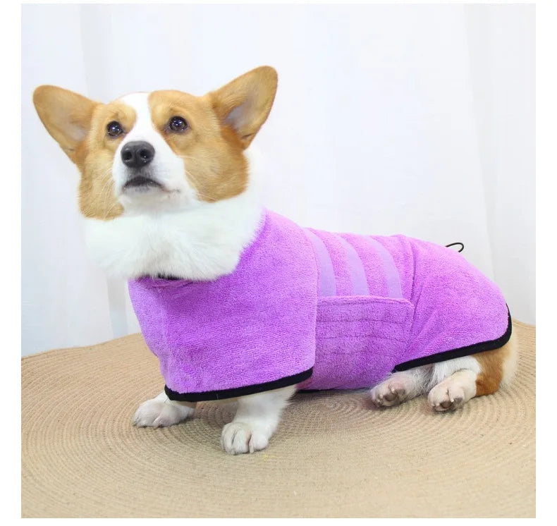 A small dog wearing a purple quick-dry microfiber robe on a beige surface.