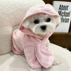 A small white dog wearing a pink multi-purpose pet bath robe.