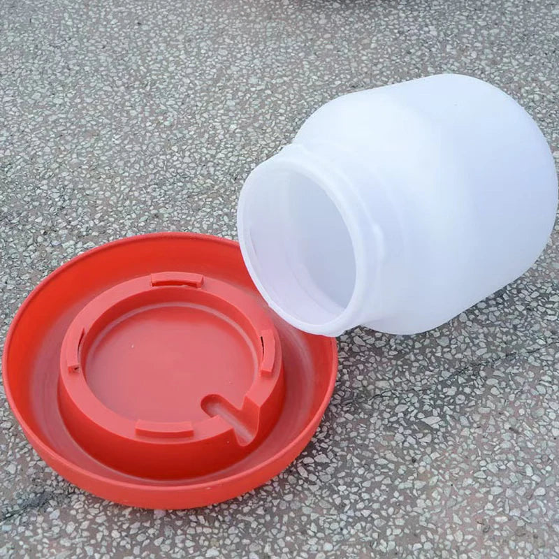 White plastic automatic poultry feeder and waterer with an orange lid placed on a gray surface.