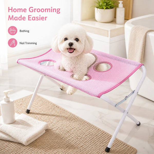 A pink foldable pet grooming hammock stand with a dog resting on it, shown next to grooming tools.