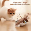 A small, fluffy cat toy resembling a bird with flapping wings and chirping features is shown on a wooden surface.