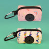 A pink zippered pouch with a black loop and a circular button is shown against a teal background.