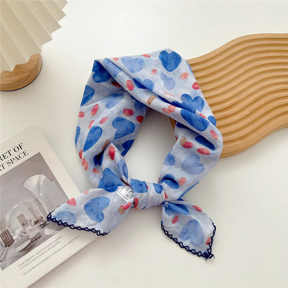Écharpes en coton bleues et roses à motifs pliées et drapées à côté d'un objet en bois.