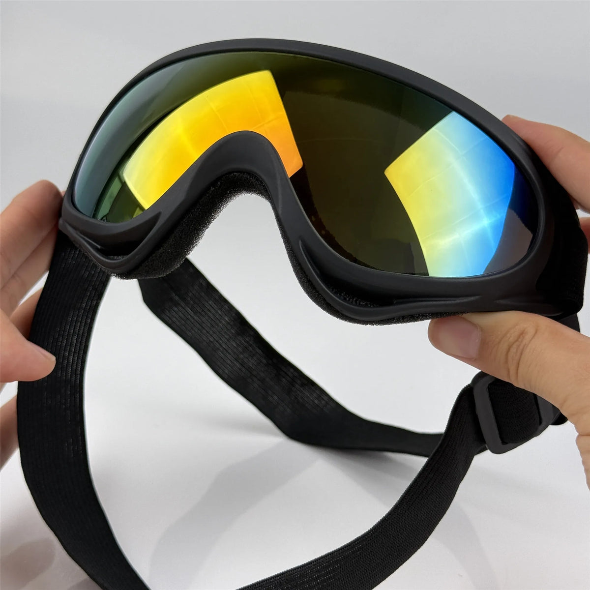A hand is holding a pair of black adjustable dog pet goggles with yellow and blue tinted lenses.
