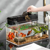 A hand is placing a section of a black external aquarium filter into a glass tank filled with gravel and aquatic plants.
