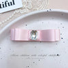 A pink satin bow hair accessory with a clear rhinestone pearl accent displayed on a white plate.