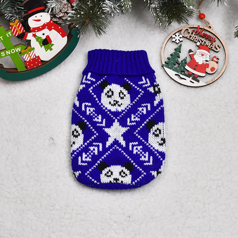 A navy blue knitted dog sweater featuring a white pattern of panda faces and stars, displayed with Christmas decorations.