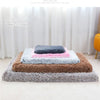 A stack of ultra plush orthopedic rectangular dog beds in shades of gray, brown, and pink on a white floor.