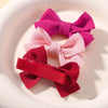 Trois nœuds papillon en ruban tricoté rose et rouge sur une assiette blanche.